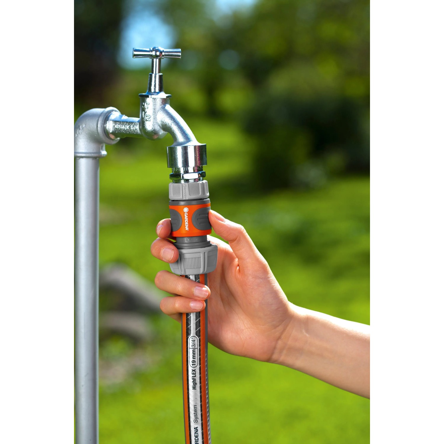Hand verbindet orange-graues Gardena Schlauchstück 19 mm (3/4) mit Wasserhahn und Gartenschlauch.