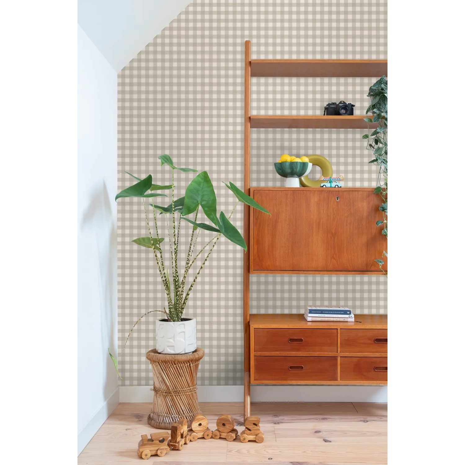 Graue Vliestapete mit Karomuster an einer Wand, daneben Pflanze und Holzregal. Dekorative Tapete.