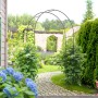 Schwarzer Furnicato Rosenbogen aus Metall im Garten, ideal für Kletterpflanzen.