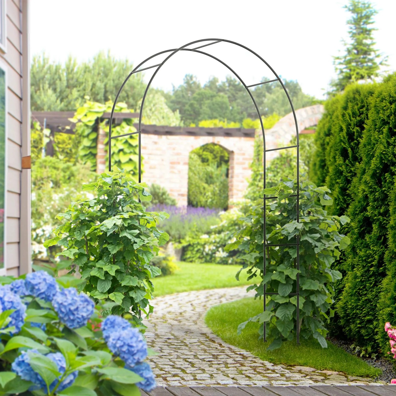 Schwarzer Furnicato Rosenbogen aus Metall im Garten, ideal für Kletterpflanzen.