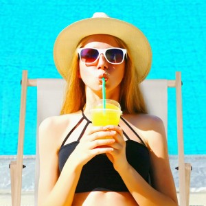 Junge Frau entspannt auf einem klappbaren Holz-Liegestuhl mit hellem Stoff am Pool. Perfekt für Garten & Strand.