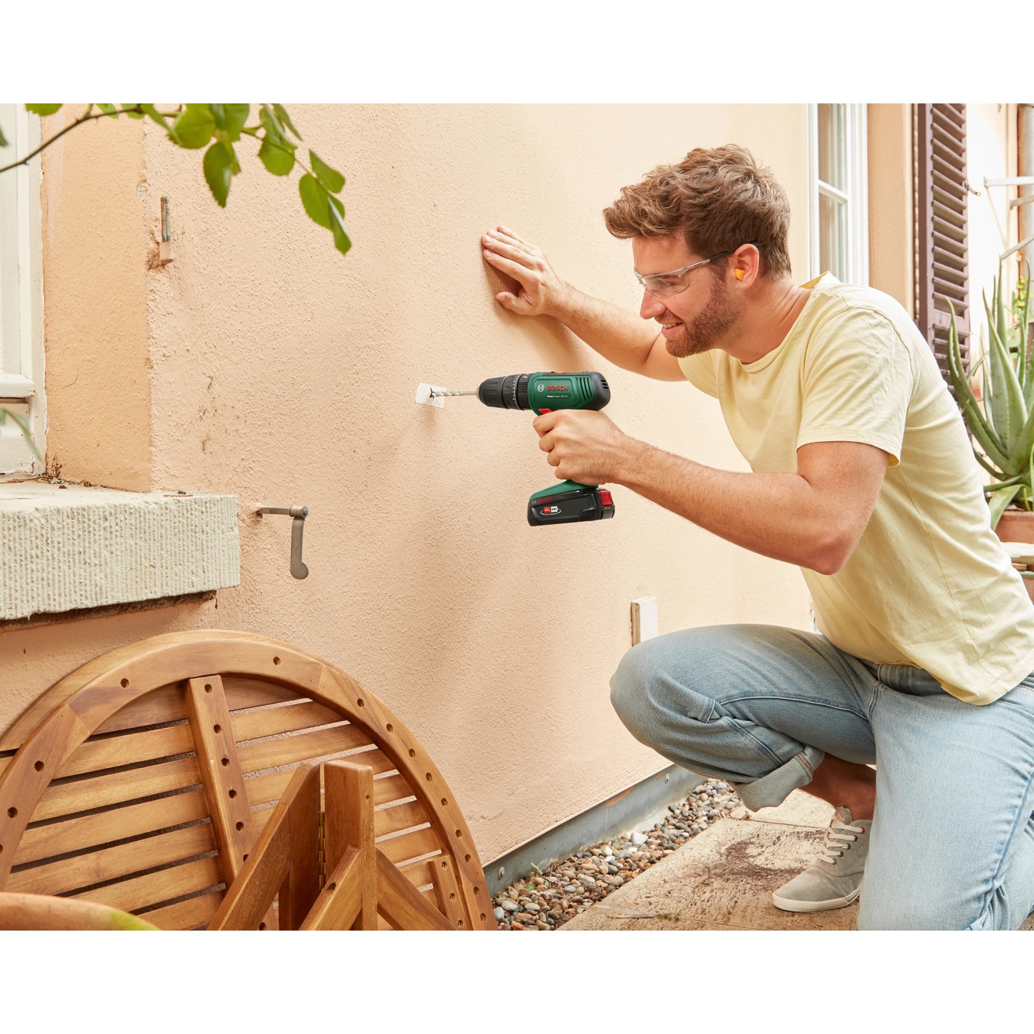 Mann bohrt mit dem Bosch 18V Akku-Schlagbohrschrauber EasyImpact 18V-40 in eine Wand.
