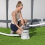 Frau installiert Bestway Polysphere Filterpumpe für Pool auf Rasen. Graue Pumpe mit Schläuchen für sauberes Wasser.