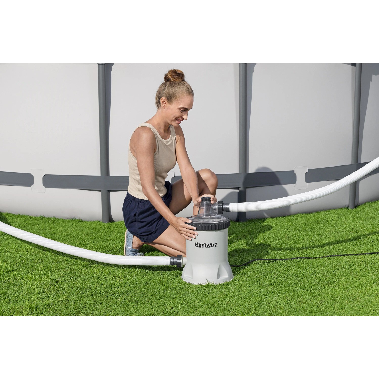Frau installiert Bestway Polysphere Filterpumpe für Pool auf Rasen. Graue Pumpe mit Schläuchen für sauberes Wasser.