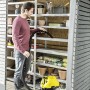 Mann saugt mit Kärcher Akku-Mehrzwecksauger WD 3 Battery Premium Set eine Regalsystem im Gartenhaus.
