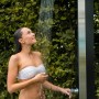 Frau unter Summer Fun Exquisit Solardusche aus Edelstahl mit Glasfront im Garten.