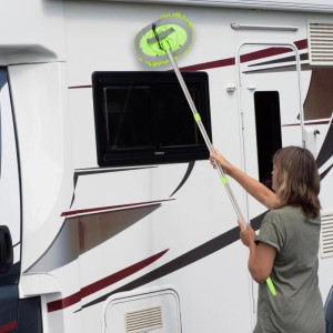 Frau reinigt Wohnmobil mit hellgrünem Autowaschmopp und langem silbernen Teleskopstiel. Autozubehör für effiziente Reinigung.