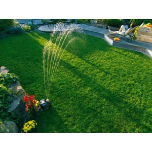 Gardena Comfort Vielflächenregner AquaContour bewässert Rasenfläche, Person entspannt im Hintergrund.