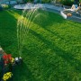 Gardena Comfort Vielflächenregner AquaContour bewässert Rasenfläche, Person entspannt im Hintergrund.