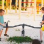 AXI Drehbare Wippe in Anthrazit/Creme mit zwei Kindern auf einem Spielplatz. Schaukeln & Wippen für Kinder.