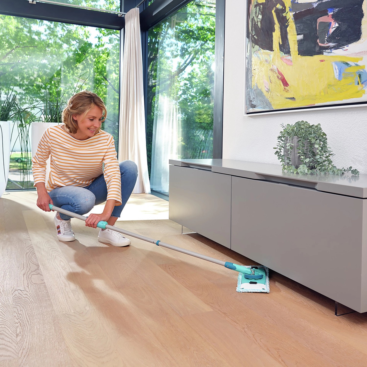 Frau wischt Boden mit Leifheit Clean Twist M Ergo Bodenwischer-Set unter Möbeln.