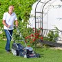 Schwarzer Relaxdays Rosenbogen mit Bank (Eisen). Mann mäht Rasen davor.