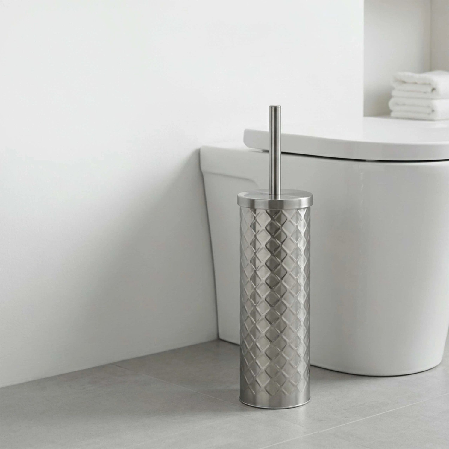Moderne silberne WC-Bürstengarnitur aus Metall mit strukturiertem Halter und langem Griff, neben einer weißen Toilette im Bad.