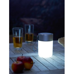 LED-Tischleuchte mit Bluetooth-Lautsprecher auf Gartentisch, Äpfel und Getränke im Hintergrund.