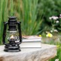 Mattschwarze Feuerhand Sturmlaterne Baby Special 276 auf Holzbank mit Büchern und Blumen im Hintergrund.