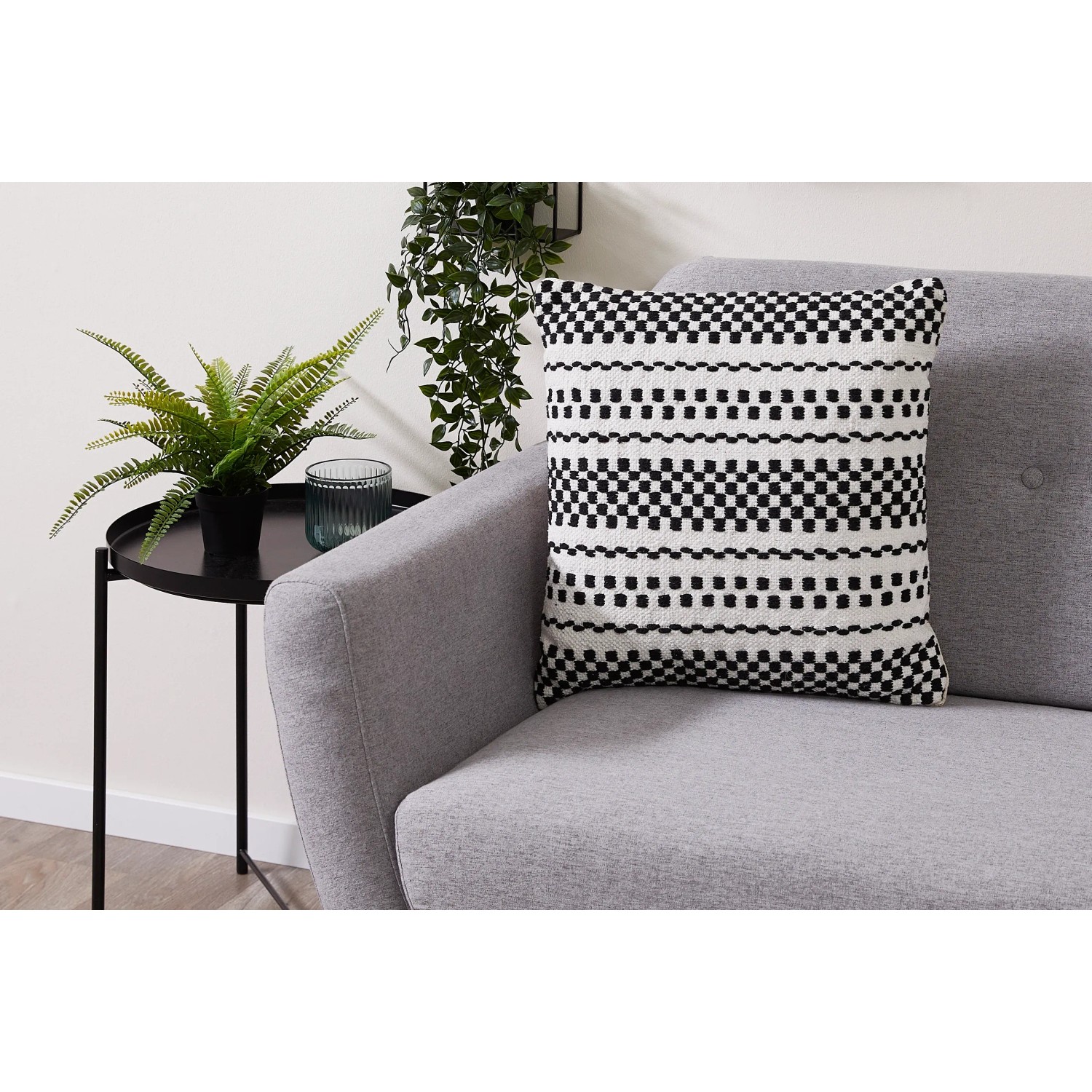 Dekoratives Andiamo Kissen Malena in Schwarz-Weiß mit geometrischem Muster auf grauem Sofa.
