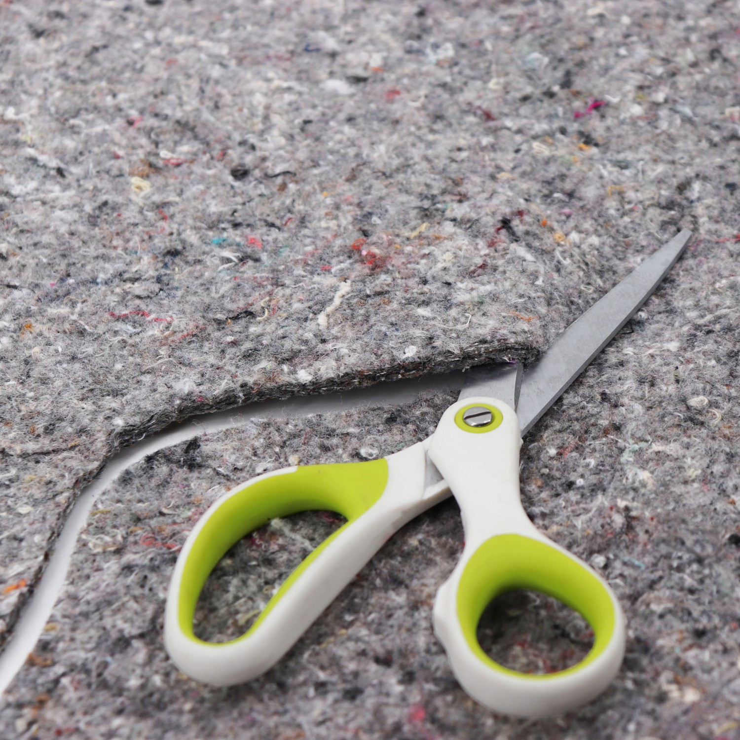 Graues Aquagart Teichvlies 1000g wird mit einer Schere zugeschnitten. Schutzvlies für Teichfolien.