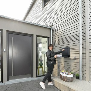 Anthrazitfarbener Burg-Wächter Briefkasten Seattle 848 mit Zeitungsbox an Hauswand, Frau wirft Post ein.
