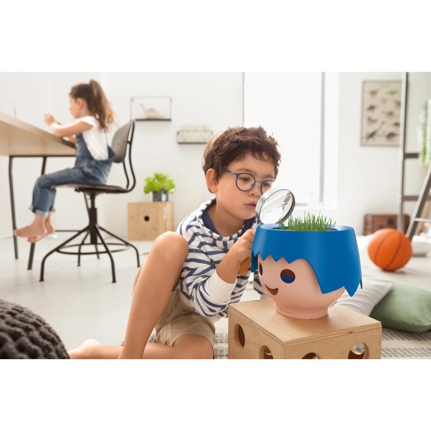 Kind betrachtet Lechuza Ojo Pflanzgefäß (Ocean Blue) mit Lupe. Spielerische Pflanzenpflege im Kinderzimmer.