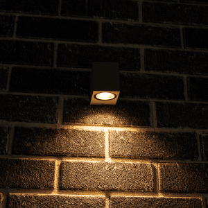 Graue, eckige LED Außenwandleuchte mit warmweißem Licht an einer Backsteinwand.