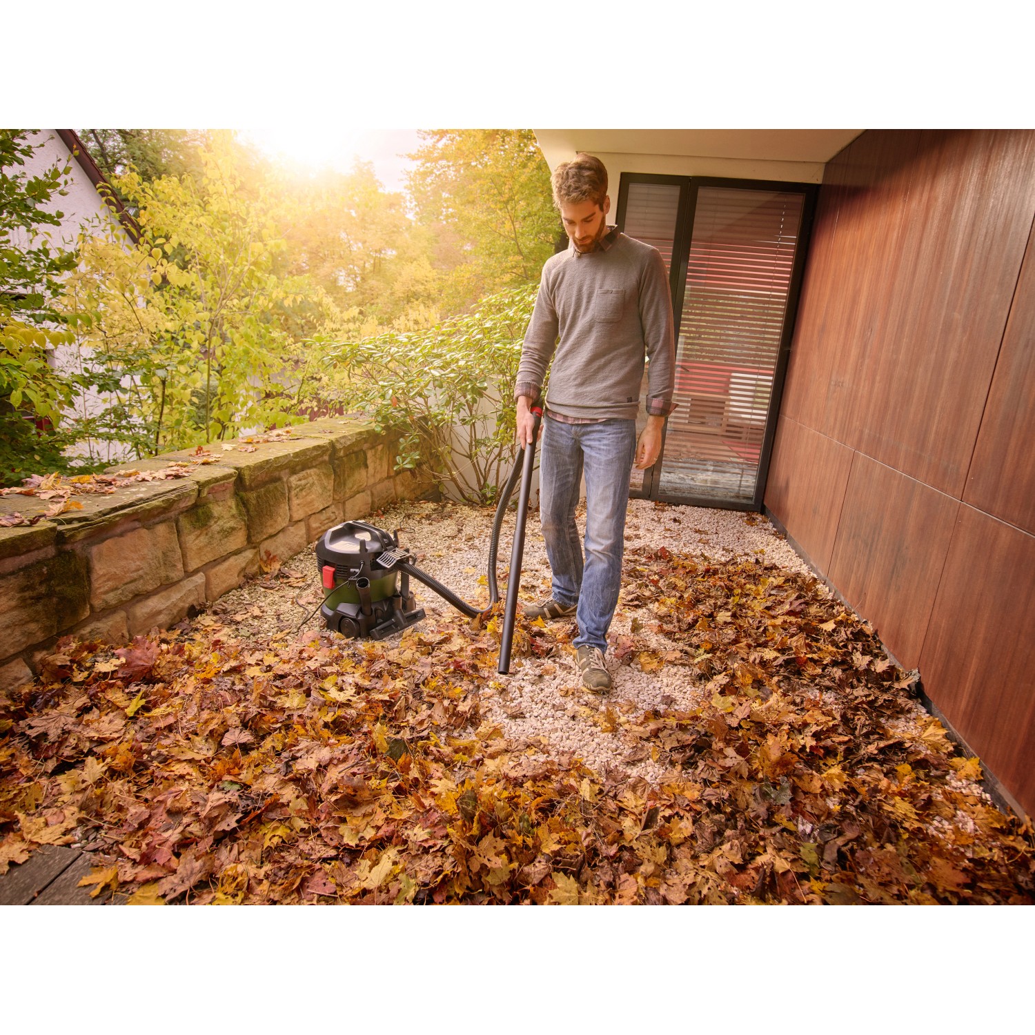 Mann saugt Laub mit dem Bosch UniversalVac 15 Nass- und Trockensauger im Außenbereich.