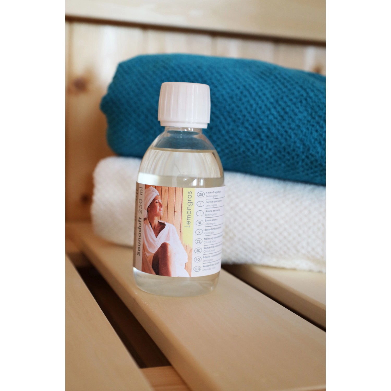 Karibu Saunaduft Lemongras, 250ml Flasche auf Holzbank vor Handtüchern.