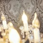 Nahaufnahme: Dunkelgraue Vliestapete mit Barock Ornament und Glanzeffekt hinter einer Kristall-Lampe.