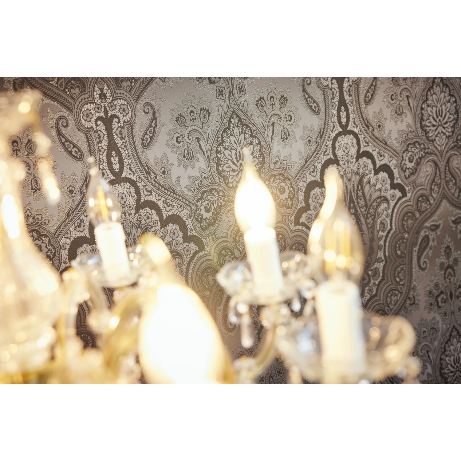 Nahaufnahme: Dunkelgraue Vliestapete mit Barock Ornament und Glanzeffekt hinter einer Kristall-Lampe.