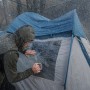Mann repariert Zeltfenster mit transparentem Tesa Ultra Power Clear Reparaturband bei Regen.