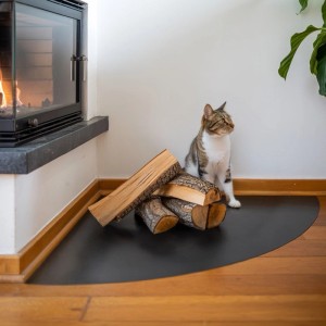 Schwarze Tulup Kaminbodenplatte aus Stahl, Viertelkreis, mit Kaminholz und Katze vor einem Kamin.