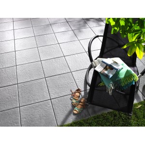 Verlegte, graue Kann Terrassenplatten Sincera 40x40 cm mit Stuhl, Decke und Schuhen auf der Terrasse.