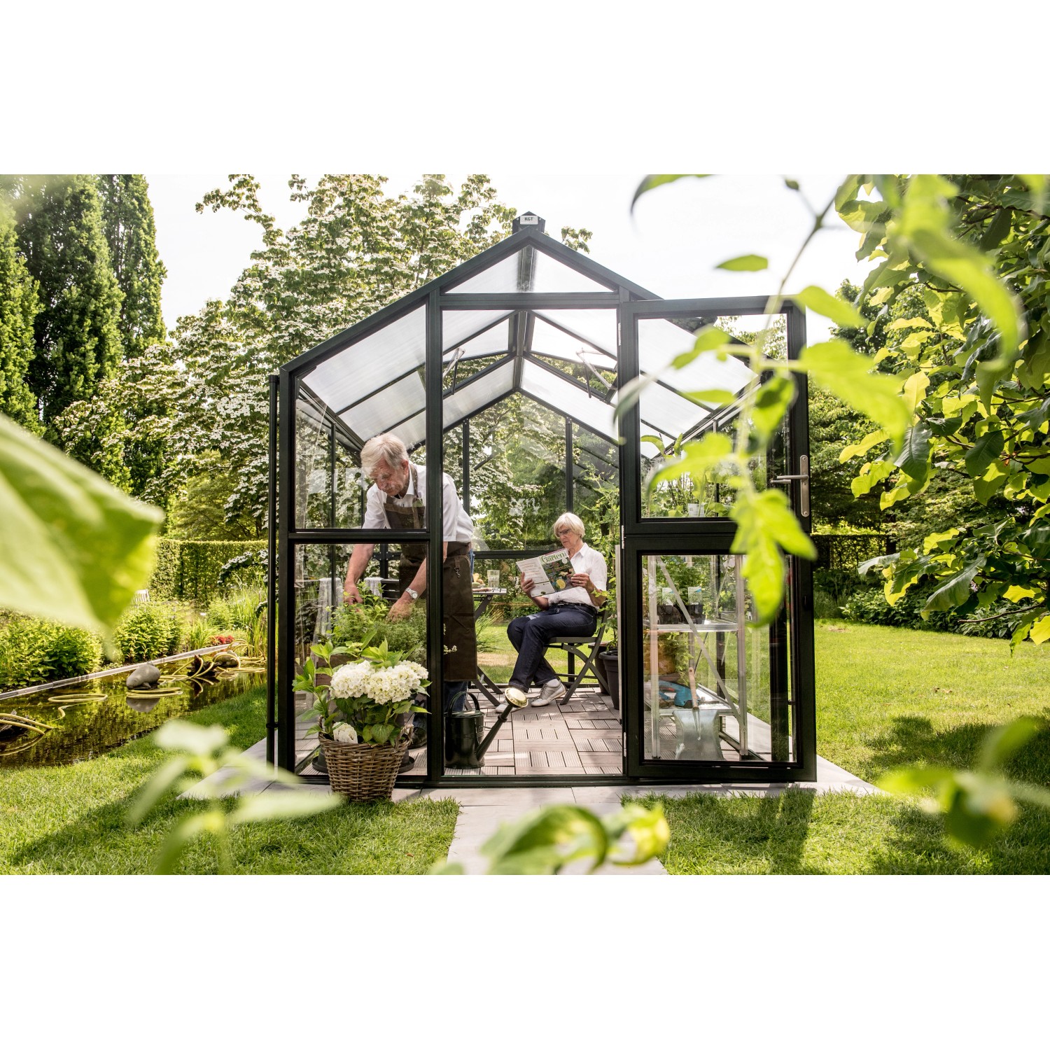 KGT Gewächshaus Galant III, tannengrün, mit Personen bei der Gartenarbeit.