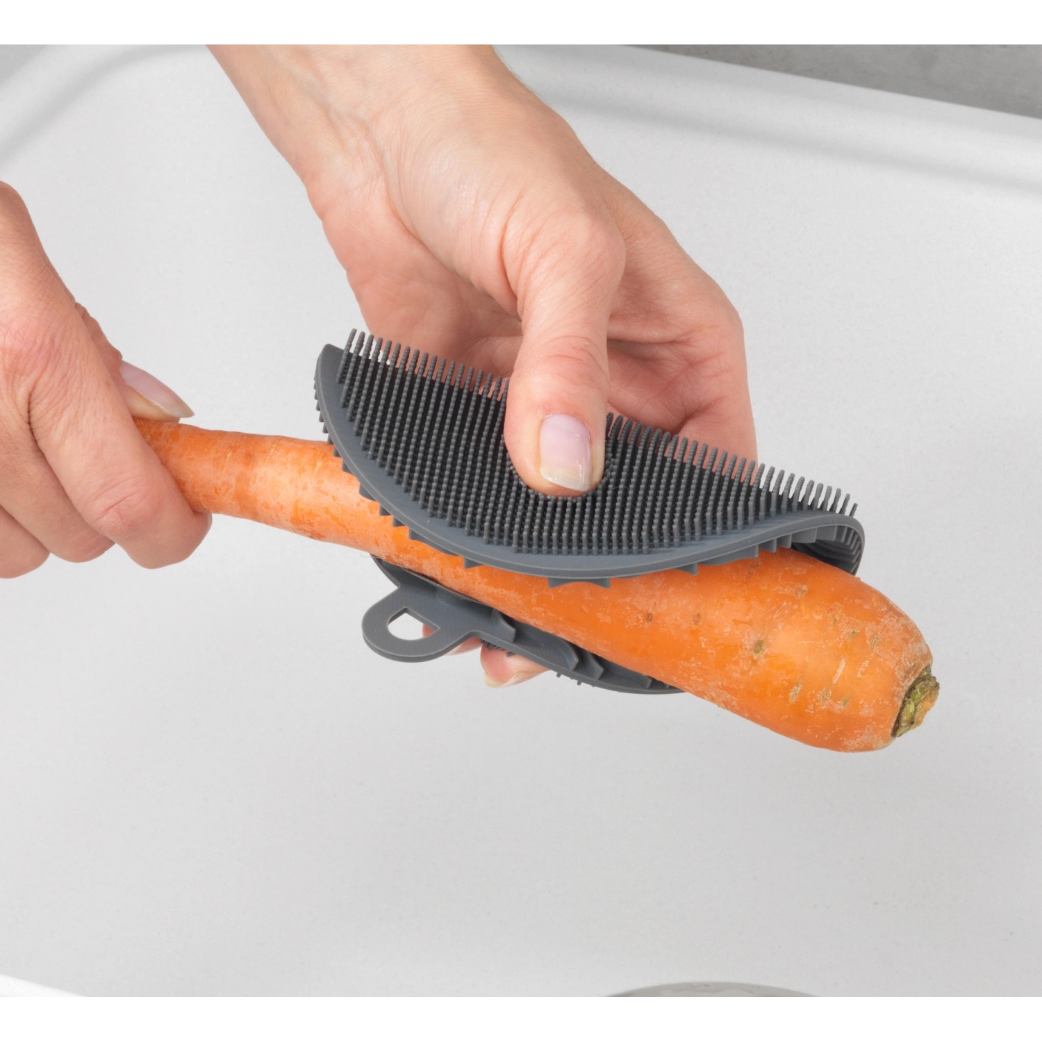 Wenko Silikon Spülschwamm 2er-Set in Aktion: Eine Hand reinigt eine Karotte mit dem grauen Küchenhelfer.