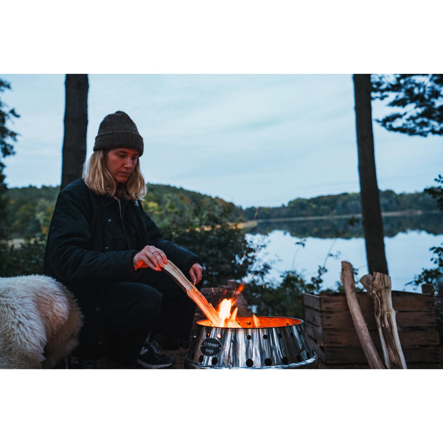 Petromax Atago Grill-Set mit Frau am Lagerfeuer im Freien. Feuerschale mit Grillspießen.