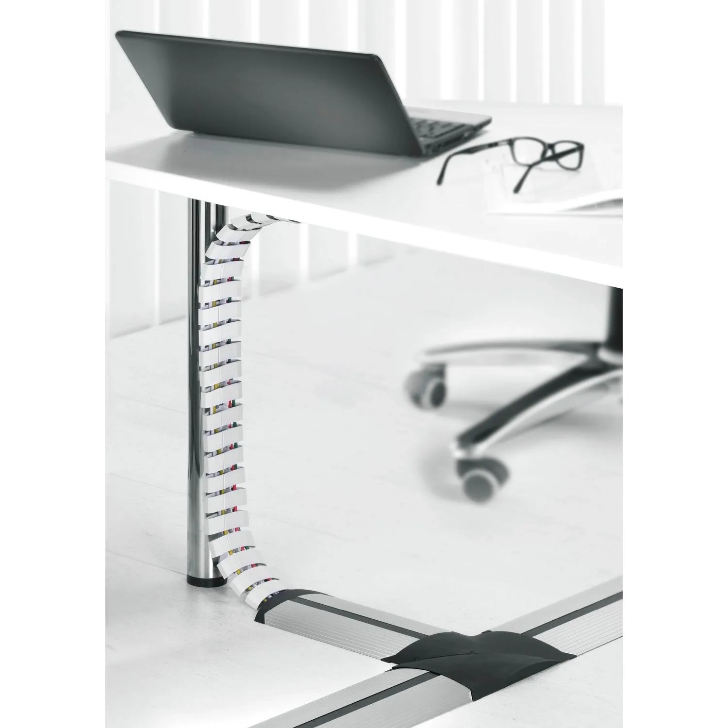 Schwarze, flexible Evoline Wirelane Schreibtisch Kabelführung unter weißem Tisch. Führt Kabel elegant zum Boden.