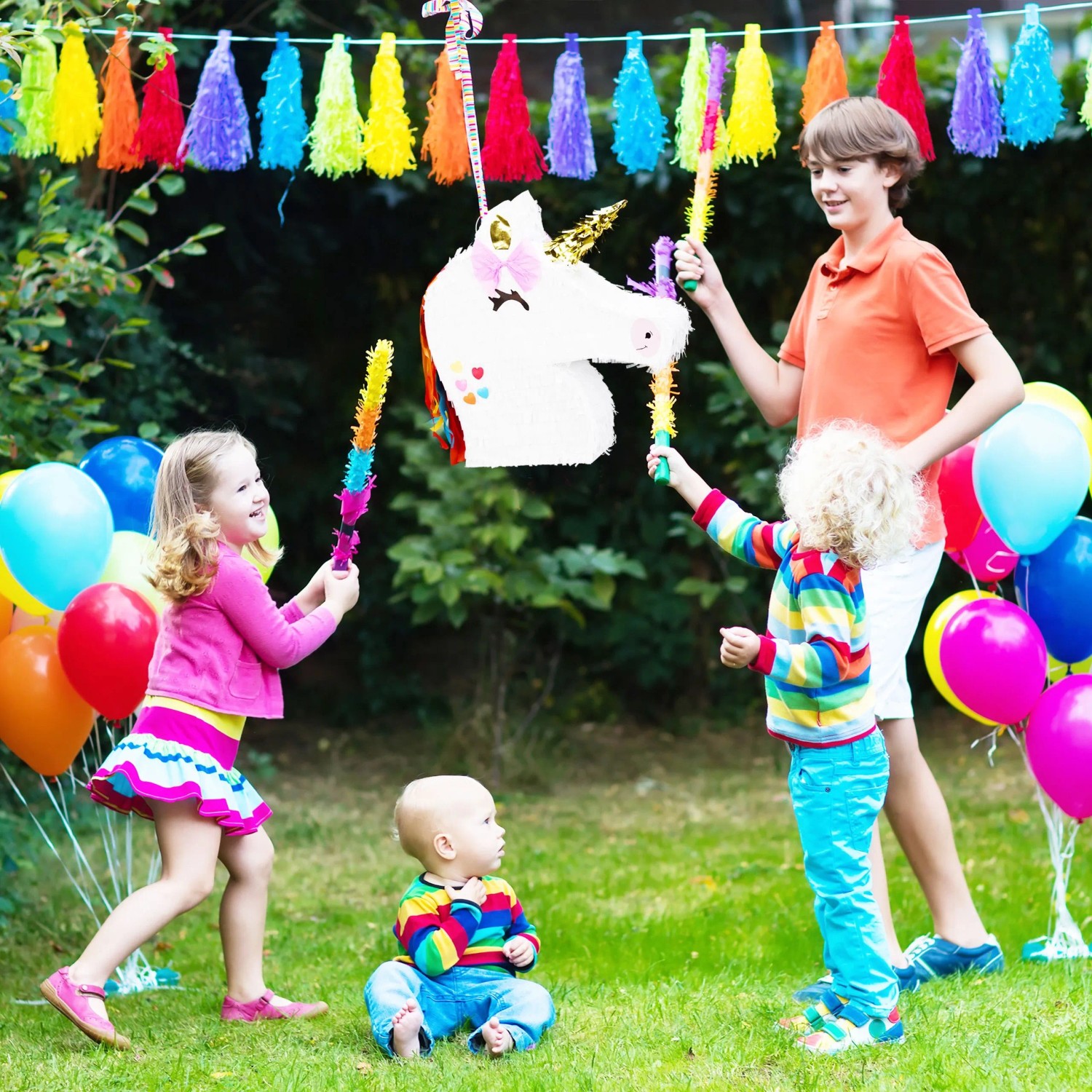 Weiße Einhorn Pinata mit bunter Mähne bei Kindergeburtstag. Kinder schlagen mit Stöcken darauf. Bunte Partydeko.