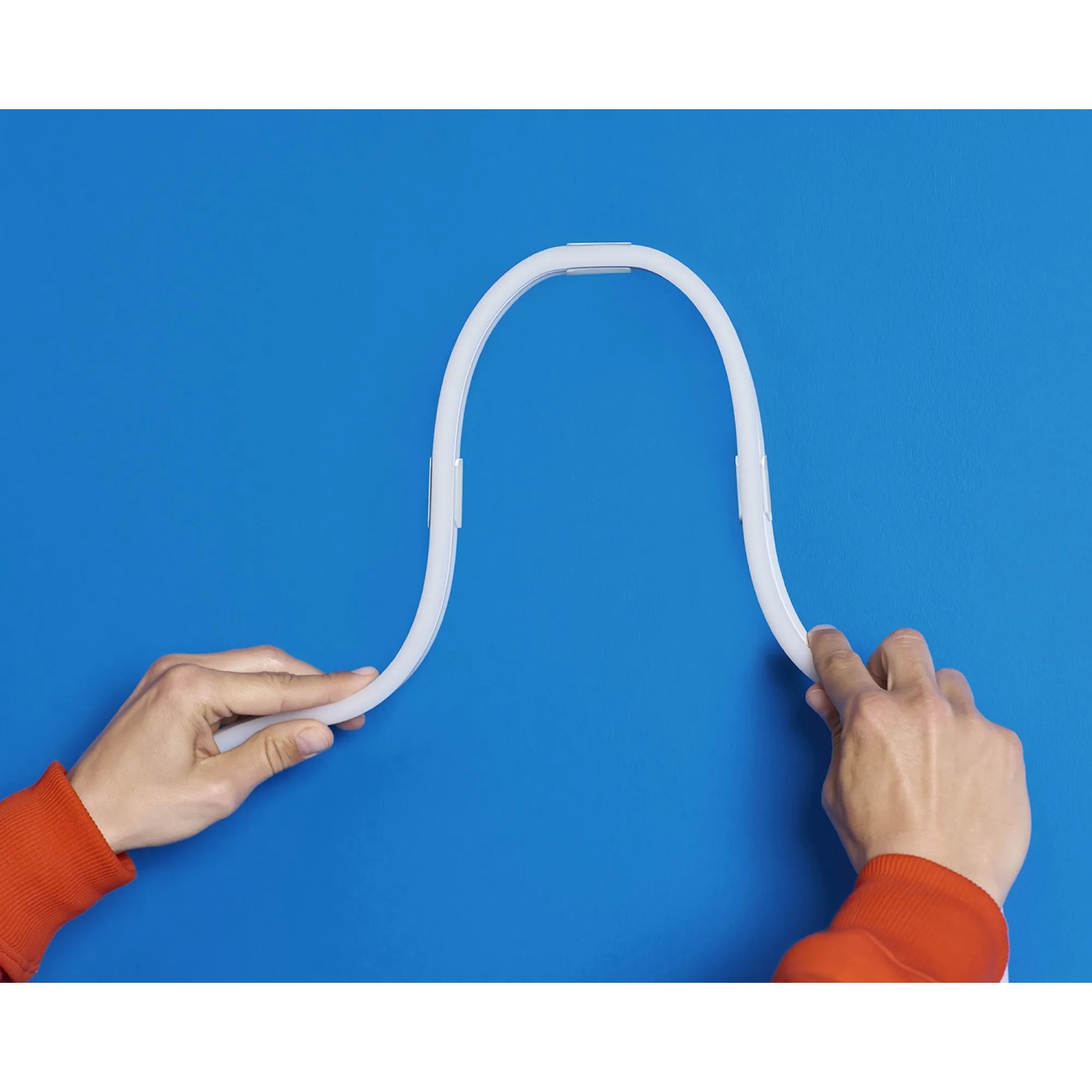 Flexibler WiZ LED Strip (3m) in Weiß, der von Händen vor blauem Hintergrund gebogen wird.