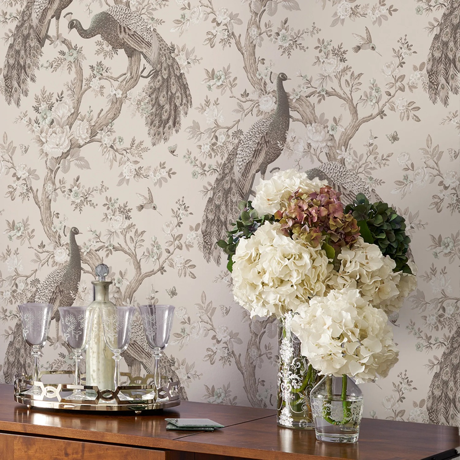 Laura Ashley Vliestapete Belvedere Soft Truffle mit Pfauenmuster und Blumen auf beiger Wand.