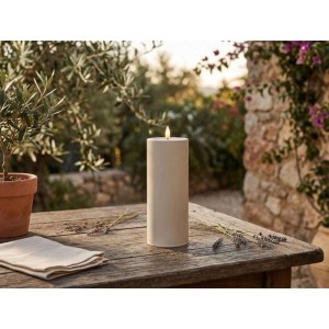 Cremefarbene Flower Power LED-Outdoor-Kerze Niumi auf rustikalem Holztisch im Garten, mit flackerndem warmweißem Licht.