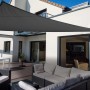 Anthrazitfarbenes Floracord Dreiecksonnensegel (460 cm) über einer Terrasse mit Gartenmöbeln.