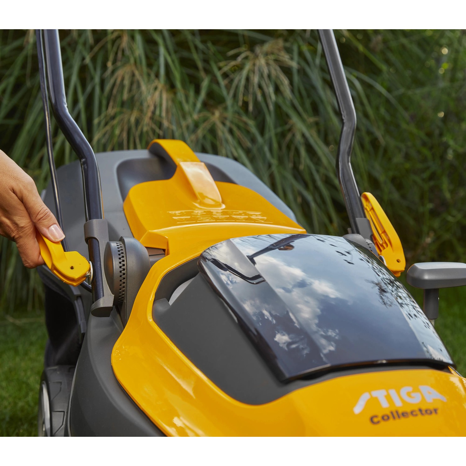 Stiga Akku-Rasenmäher Collector 136e: Detailaufnahme des gelb-grauen Mähers mit Hand am Griff.