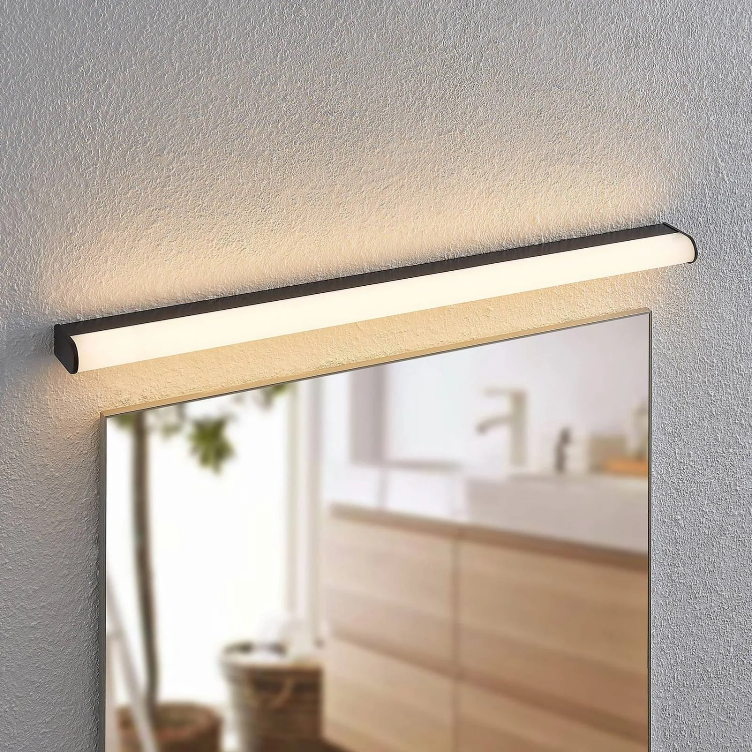 Schwarze, moderne Lindby LED Wandleuchte Ulisan aus Aluminium über einem Spiegel im Bad. Spritzwassergeschützt.
