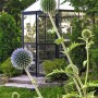 Sechseckiges Palram Canopia Oasis Gewächshaus mit Kugelblumen im Garten.