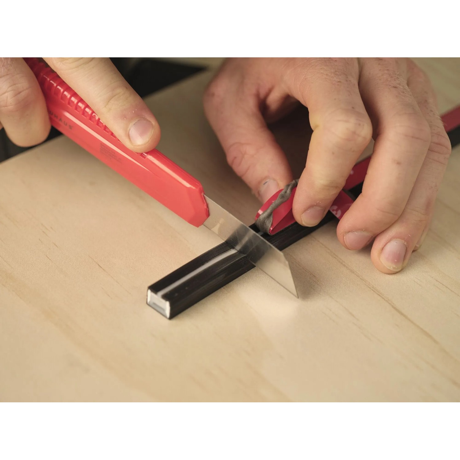 Hände kürzen schwarzen OSRAM Acoustic LED Streifen mit rotem Cuttermesser auf Holz. Kürzbarer LED-Streifen.