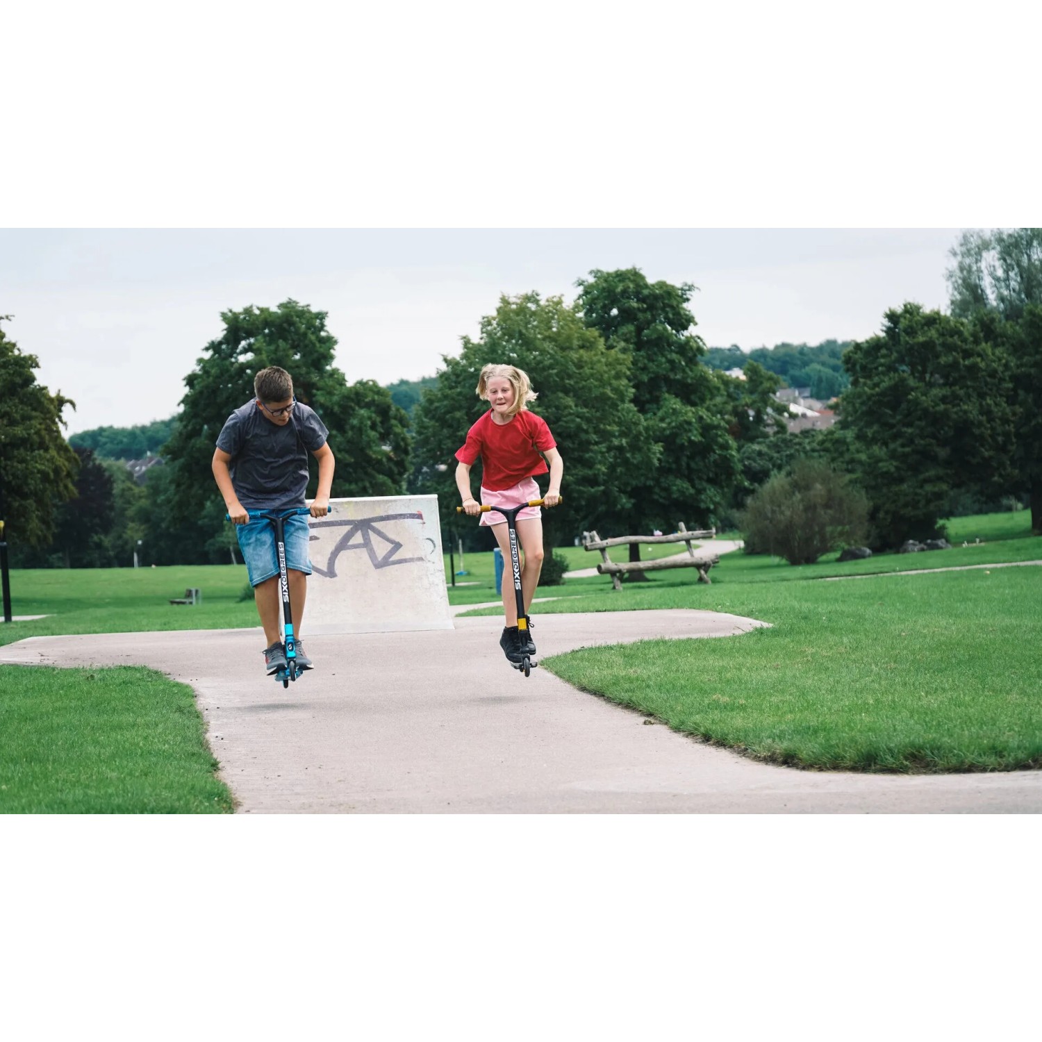 Zwei Kinder springen mit blauen Six Degrees Stuntscootern im Skatepark.