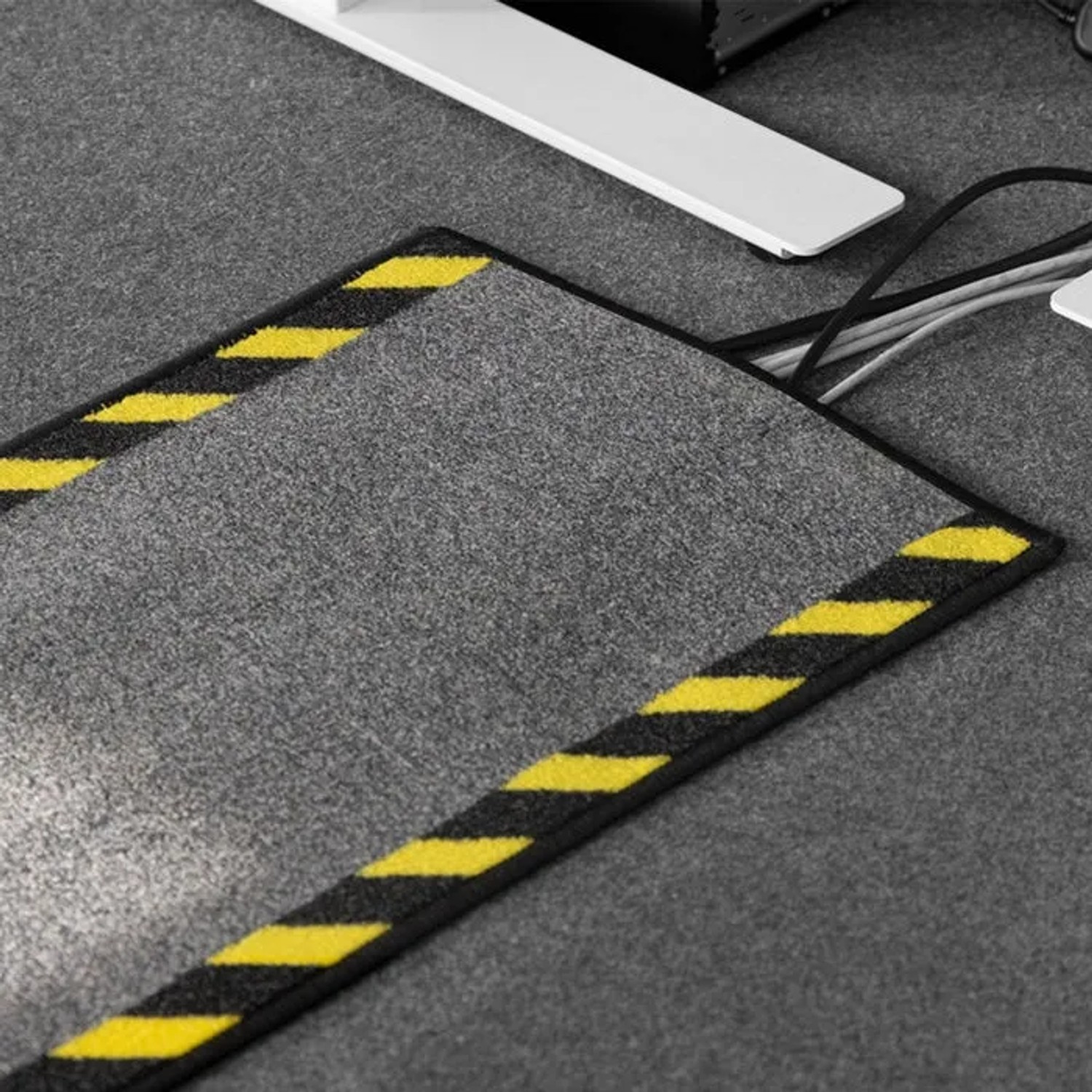 Graue Karat Kabelmatte mit schwarz-gelber Warnumrandung unter einem Schreibtisch mit Kabeln.