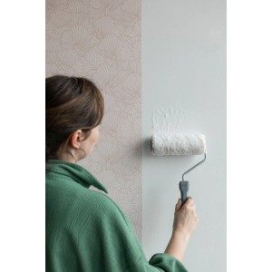 Frau streicht Wand mit Wallpro großer Walze 18 cm. Tapezierwerkzeug für Farbe und Tapetenkleister.