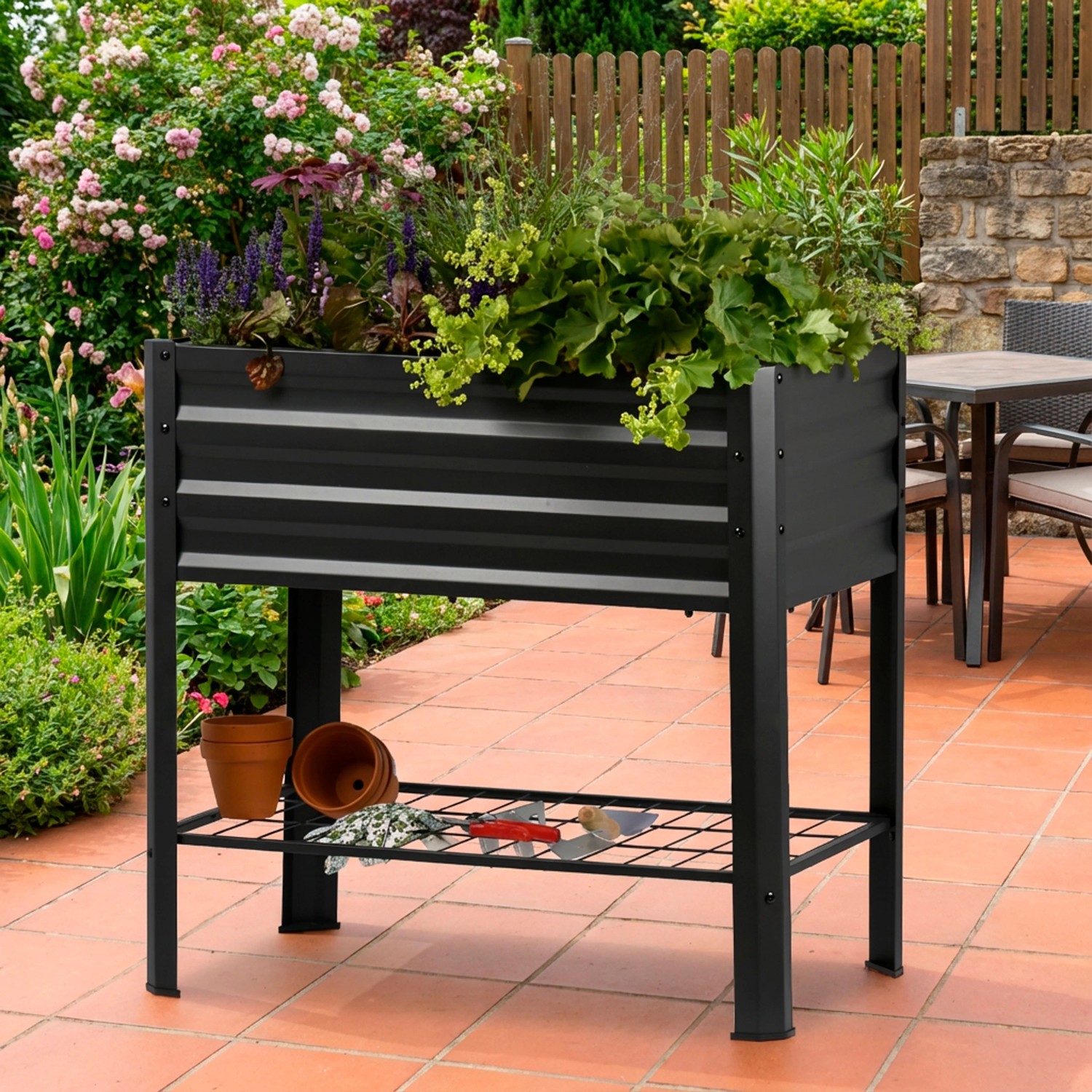 Schwarzes Metall-Hochbeet Kubus auf Stelzen mit Ablagefläche, bepflanzt mit Kräutern und Blumen.