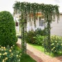 Schwarzer Costway Rosenbogen aus Metall, bewachsen mit Kletterpflanzen, als Rankhilfe im Garten.