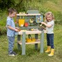 Fröhliche Kinder spielen mit der bunten Smoby Matschküche Life im Garten. Inkl. Zubehör.